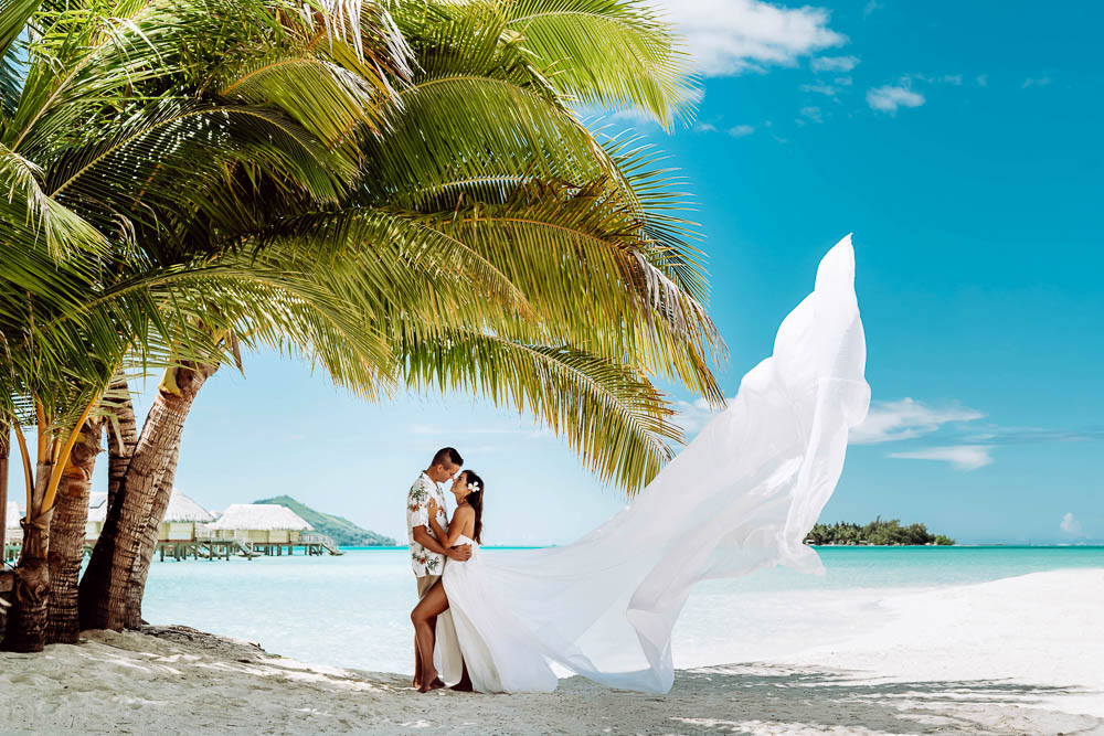 Couple faisant une séance photo flying dress sur la plage avec une longue robe blanche.