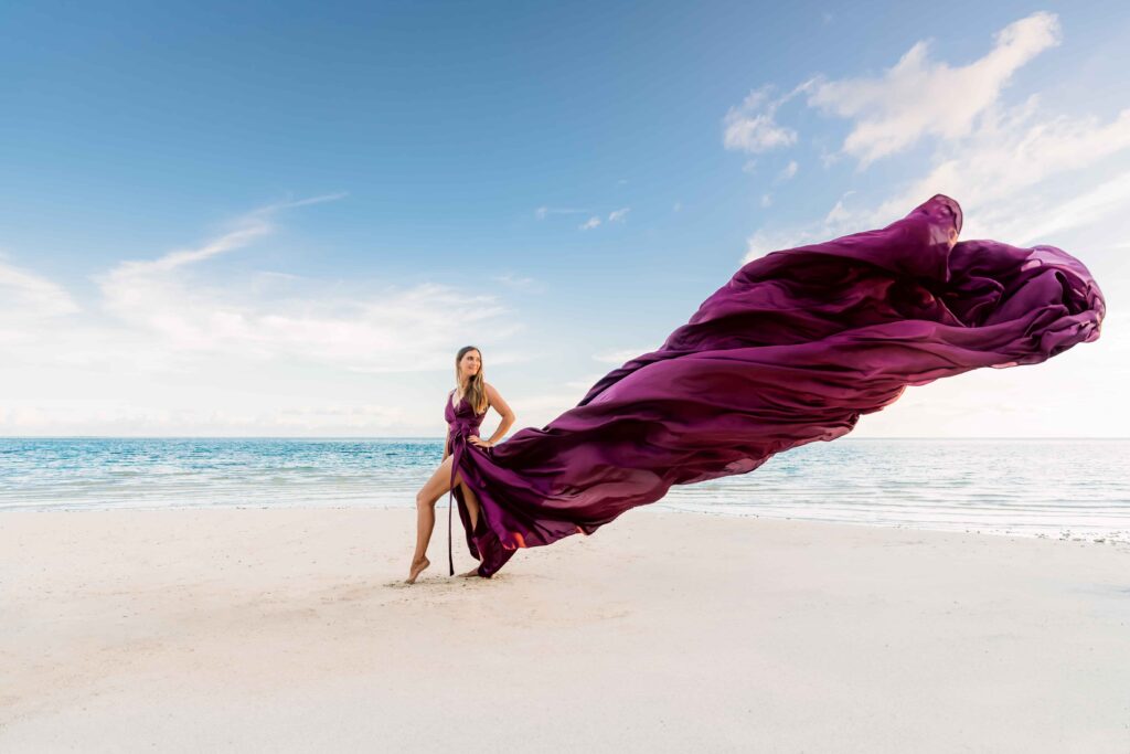 Séance photo de flying dress sur la plage. La modèle porte une longue robe violette