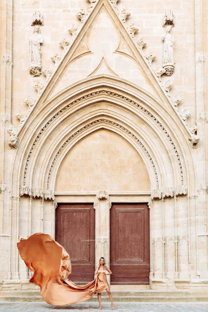 Photo d'une femme blonde habillée d'une flying dress dorée devant la cathédrale de Béziers